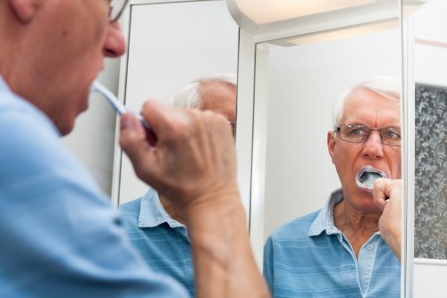 Close up of senior man reflected in mirror brushing his teeth.